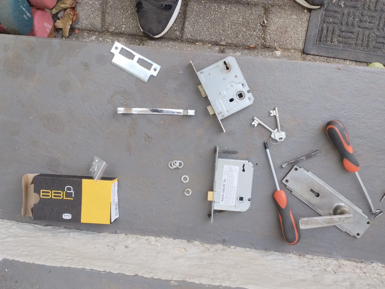 Mortice locks, keys, screwdrivers and a lock box laid out on a step during a lock replacement.